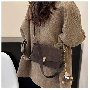 Detailed view of the dark brown suede bag with gold nut buckle and plush charm detail