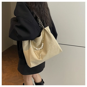 Detail of elegant beige tote bag featuring gold chain and pearl strap embellishments