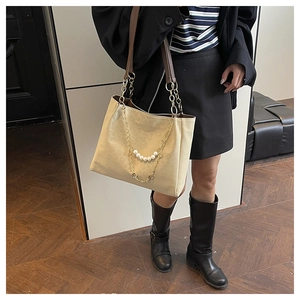 Detail of a beige tote bag with gold chain and pearl charms worn with a black blazer