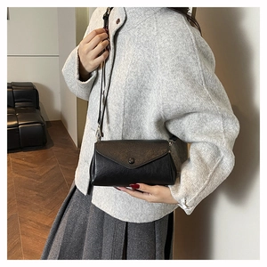 Detail of a black minimalist envelope crossbody bag with a vintage lychee texture finish