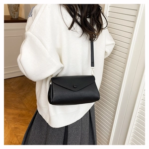 Detail shot of a black envelope crossbody bag with a round buckle and gold metal hardware