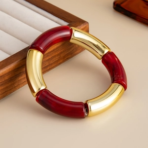 Detalle de tubos curvos de resina roja y metal dorado en pulsera elástica de moda