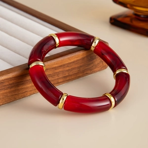 Detail of red resin bamboo bracelet with gold accents on a wooden jewelry display