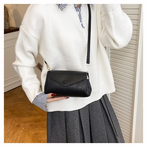 Detail of a minimalist black square crossbody bag with lychee texture and round button