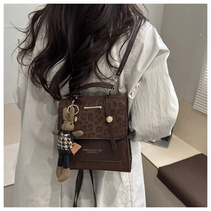 Dettaglio di zaino vintage in pelle marrone con patta leopardata e ciondolo a coniglio