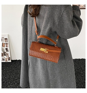 Detail van bruine tas met geweven textuur, gouden draaisluiting en elegant handvat