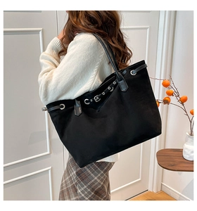 Detail of a large black suede tote bag with leather drawstring and metal eyelets on the side