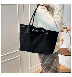 Detailed view of black tote bag with metal eyelets and leather buckle on a model