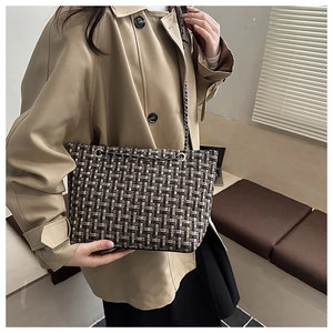 Detailed view of woven plaid tote bag with metal chain strap on woman's shoulder