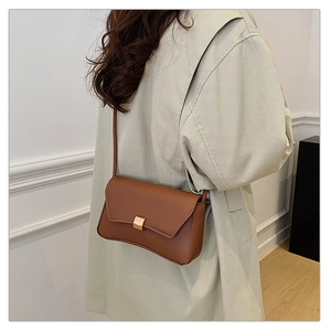 Borsa a tracolla in pelle marrone con fibbia dorata indossata da modella in cappotto