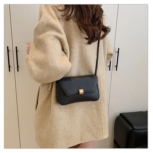 Dettaglio borsa a tracolla in pelle nera opaca con fibbia dorata su cappotto beige