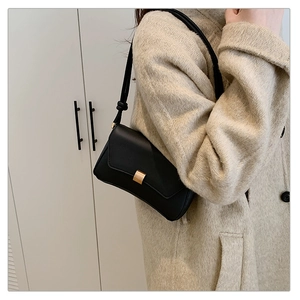 Dettaglio borsa baguette minimalista in pelle nera indossata su cappotto in lana beige