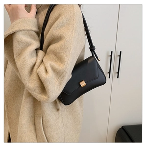Dettaglio borsa baguette nera con fibbia dorata indossata su un cappotto beige