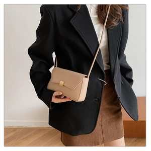 Dettaglio di una borsa a tracolla beige minimalista con fibbia metallica su una modella