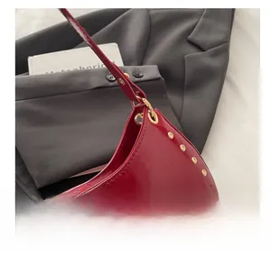Détail du sac rouge à rivets dorés posé sur un fond de costume gris foncé