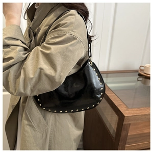 Close-up of a black glossy hobo bag with gold rivet accents worn with a khaki trench coat