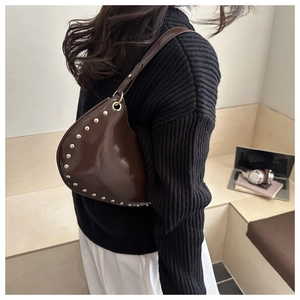 Detail of dark brown patent leather crescent bag with golden studs and metal ring strap