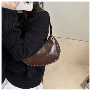 Détail du sac croissant marron foncé brillant avec des rivets dorés polis le long de la base