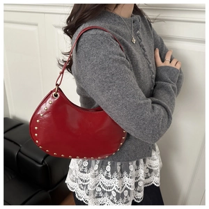Detailed close-up of a red leather crescent hobo bag with gold stud trim on model