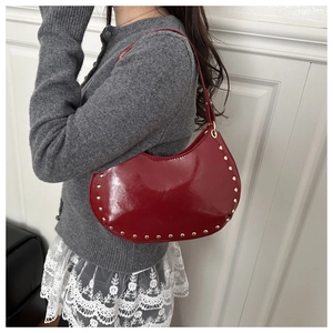Detail of dark red patent leather crescent bag with gold rivets and shiny finish