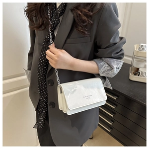 Detailweergave van witte glanzende crossbodytas met zilveren ketting en opgedrukte tekst