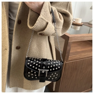 Close-up of black patent leather punk bag with silver studs and chain strap on a model