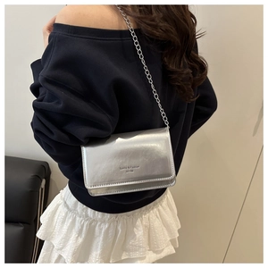 Silver glossy square crossbody bag with chain strap shown on model in modern setting