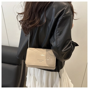 Detail van beige lakleren schoudertas met zilveren kettingriem gedragen door model