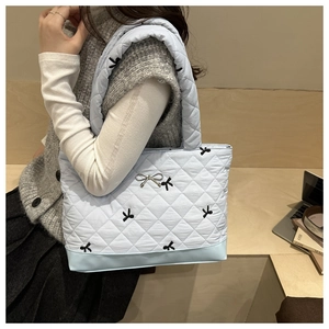 Dettaglio della borsa tote trapuntata celeste con ricamo a fiocco e ciondolo in metallo argento