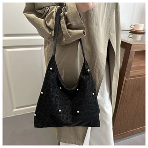 Detail of black leopard print tote bag with golden rivets worn on shoulder by a model