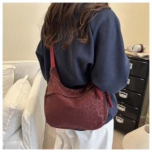 Détail d'un sac bandoulière bordeaux imprimé léopard avec tirette tissée porté par le mannequin