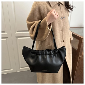 Detail of black leather pleated cloud tote bag featuring FASHION BAGS text on a camel coat