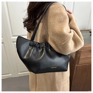 Detail view of a black ruched shoulder bag with gold text on a wool coat outfit