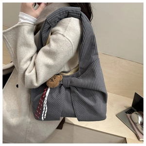 Detail der grauen Cord-Schultertasche mit großer Schleife und kleinem Bären-Anhänger