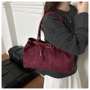 Close-up of deep red suede tote bag with smooth leather handles and gold metal buckles