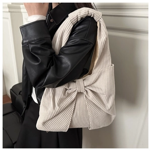 Detail der cremefarbenen Cord-Schultertasche mit großem Schleifendesign und breitem Gurt