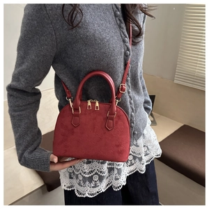 Detail of red shell-shaped handbag featuring embossed clover patterns and gold metal zippers