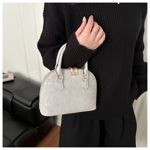 Detail of grey shell bag featuring embossed clover patterns and gold metal zipper