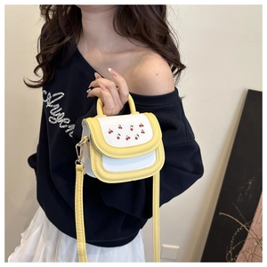 Detail of yellow cherry print mini crossbody bag on a model wearing casual white sweatshirt