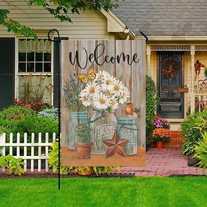 Outdoor garden flag with blue mason jar and daisies on a white fence lawn background