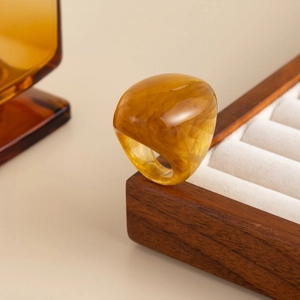 Detailed view of wide amber resin ring with marble texture on wooden display stand