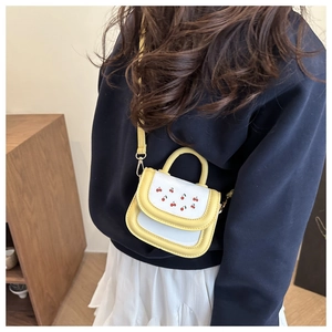 Detail of a mini yellow and white crossbody bag with cute red cherry pattern and strap
