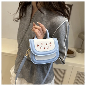 Detail of mini blue and white crossbody bag featuring cute red cherry print and gold clasp