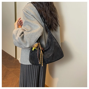 Détail du sac demi-lune noir en daim avec pompons décoratifs porté à l'épaule