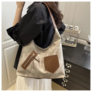 Detail of canvas tote bag showing dark brown leather straps and front zip pocket