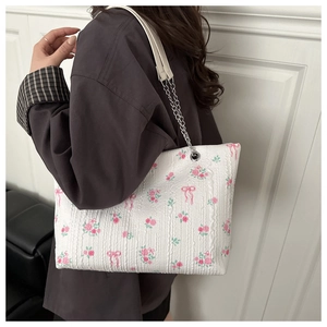 Detail of floral tote bag featuring pink rose and bow prints with a silver chain strap