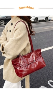 Detail of burgundy glossy leather tote bag featuring decorative straps and metal buckles