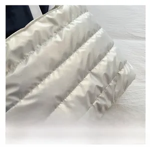 Close-up of glossy white quilted fabric with horizontal stitching on a fashion tote bag