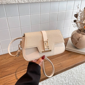Sac bandoulière chic en cuir crème et paille avec boucle dorée sur table en bois