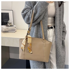 Detail of a minimalist beige leather tote bag with a decorative printed silk scarf on the strap